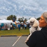 Jessica holding her white poodle at an outdoor craft fair with tents behind her